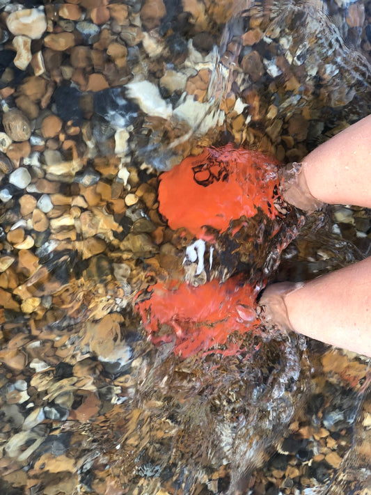 Orange neoprene water shoes partially submerged in water on a rocky surface