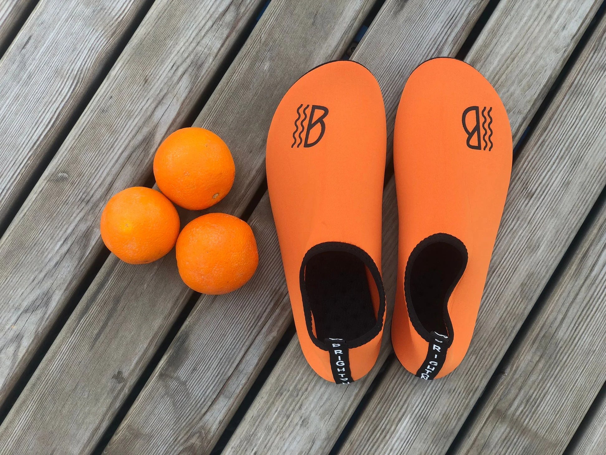 Orange neoprene water shoes on a wooden surface, accompanied by three orange balls.